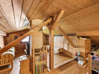 Discover this charming attic room, featuring a cozy sleeping area with a striped duvet and a rustic wooden beam structure.