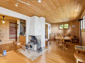 Experience rustic charm in this inviting living and dining area, featuring a prominent stone fireplace and warm wooden ceilings and walls.
