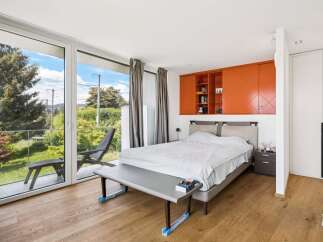 Experience modern living in this serene bedroom featuring a spacious king-size bed and vibrant orange built-in cabinetry for ample storage and display.