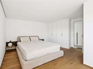 This modern bedroom features a comfortable bed with crisp white linens and plush pillows, complemented by a minimalist bedside table with a globe lamp.