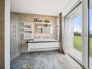 Experience modern luxury in this stunning bathroom featuring a sleek double vanity with a backlit mirror and a spacious glass-enclosed shower.