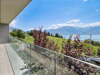 Experience breathtaking panoramic views from this stunning property, featuring a spacious balcony with a modern glass railing.