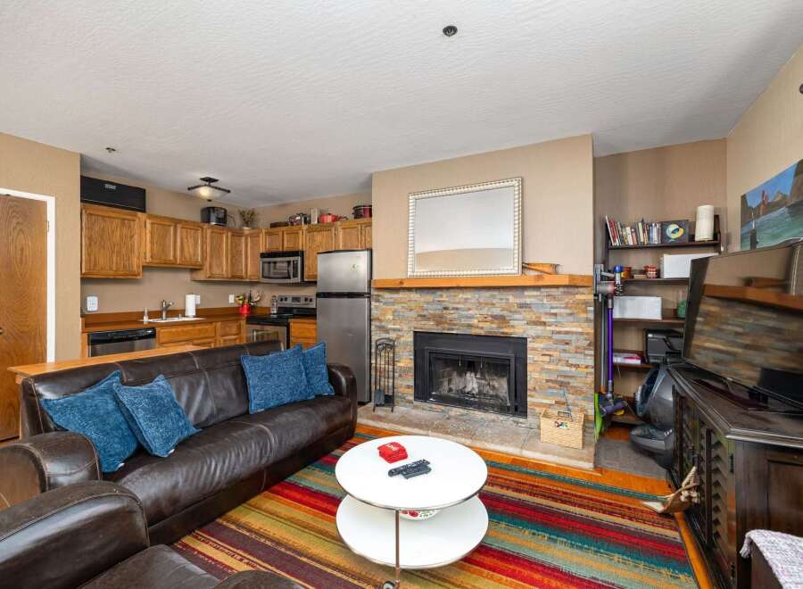 Cozy living room featuring a plush leather sofa with blue accent pillows, centered around a striking stone fireplace.