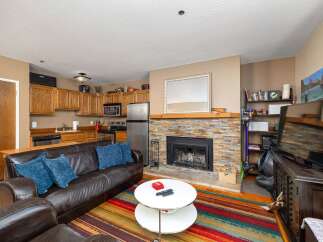 Cozy living room featuring a plush leather sofa with blue accent pillows, centered around a striking stone fireplace.