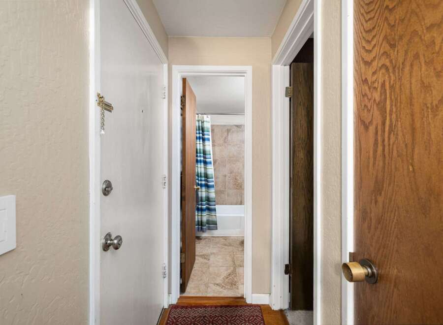 Step into this charming hallway, offering access to a bright bathroom with a blue and green striped shower curtain and tiled walls.