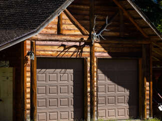 Rustic charm meets functionality in this log cabin garage, featuring two spacious garage doors and a unique deer antler mount above.