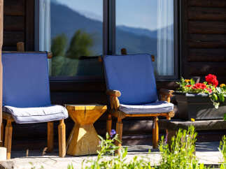 Enjoy the serene mountain views from this charming log cabin's porch, complete with comfortable seating and a rustic wooden side table.