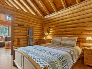 Experience rustic charm in this cozy log cabin bedroom, featuring a comfortable bed adorned with a patterned duvet and matching pillows.