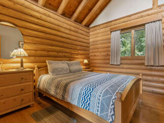 Experience rustic charm in this cozy log cabin bedroom, featuring a comfortable bed with a patterned comforter and a wooden dresser with a decorative lamp.