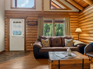 Experience rustic charm in this cozy log cabin living room, featuring a plush brown sofa adorned with decorative pillows and a unique wooden trunk coffee table.