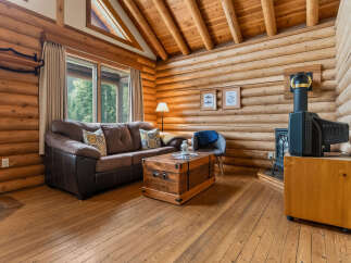 Experience rustic charm in this cozy log cabin living room, featuring a plush leather sofa, a unique wooden trunk coffee table, and a wood-burning stove for ultimate warmth.