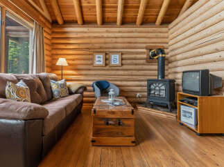 Experience rustic charm in this cozy log cabin living room, featuring a plush brown sofa perfect for relaxing by the cast iron stove.