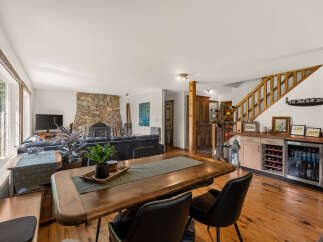 Experience rustic charm in this open-concept living space, featuring a striking stone fireplace and a warm wooden dining table perfect for gatherings.
