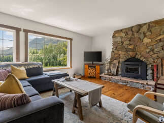Experience breathtaking mountain views from this cozy living room, featuring a stunning stone fireplace and a comfortable sectional sofa.