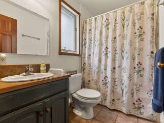 This charming bathroom features a floral shower curtain, a wooden vanity with a white sink, and a toilet.