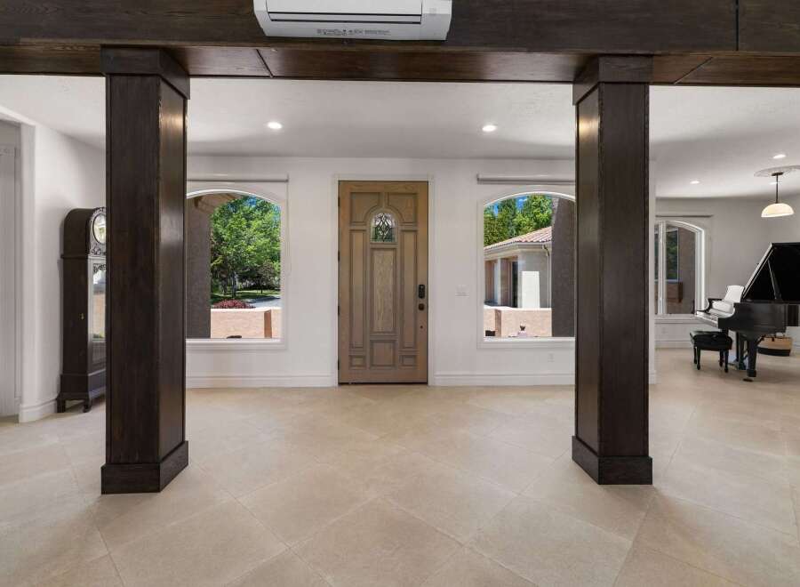 Step into a grand foyer featuring a beautiful wooden front door flanked by arched windows offering picturesque views of the lush outdoors.