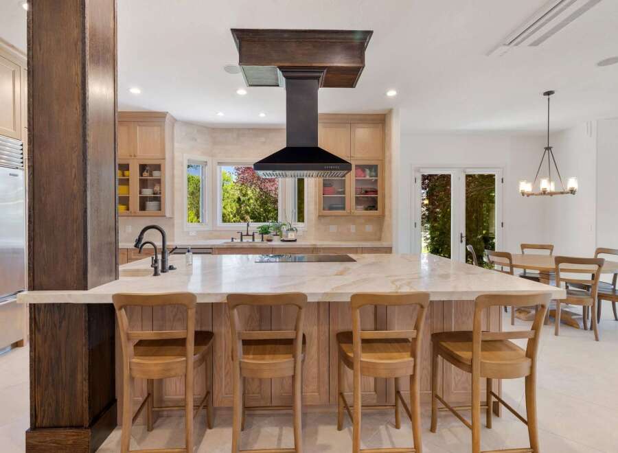 Experience luxury in this stunning kitchen, featuring a large marble island with seating and a sleek black range hood.