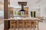 Experience luxury in this stunning kitchen, featuring a large marble island with seating and a sleek black range hood.