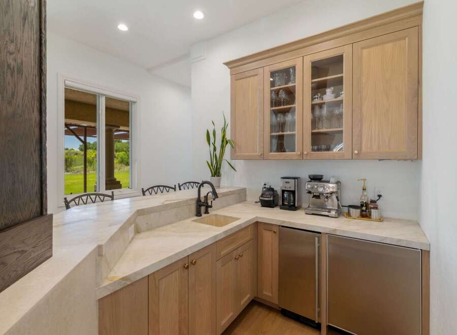 This stunning wet bar features a sleek marble countertop and backsplash, complemented by custom light wood cabinetry.