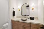 This modern bathroom features a stylish vanity with a stone countertop and a vessel sink, complemented by a large arched mirror and elegant brass sconces.