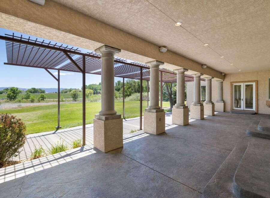 Enjoy the outdoors from this covered patio featuring elegant columns and a pergola, perfect for al fresco dining or relaxing with a view.
