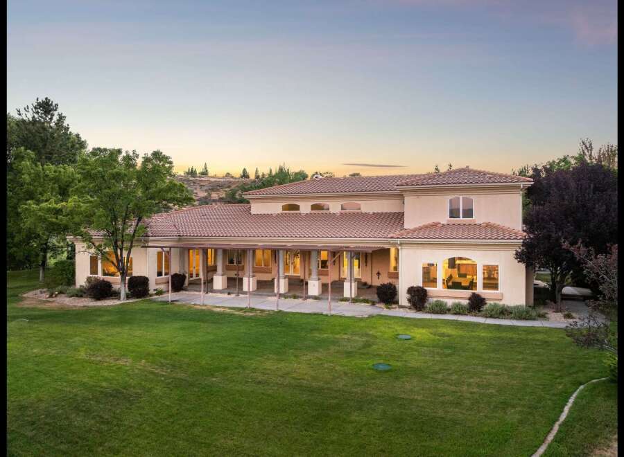 This expansive estate features a stunning stucco exterior with a classic tile roof, complemented by a long, covered veranda perfect for outdoor entertaining.