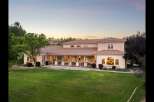 This expansive estate features a stunning stucco exterior with a classic tile roof, complemented by a long, covered veranda perfect for outdoor entertaining.