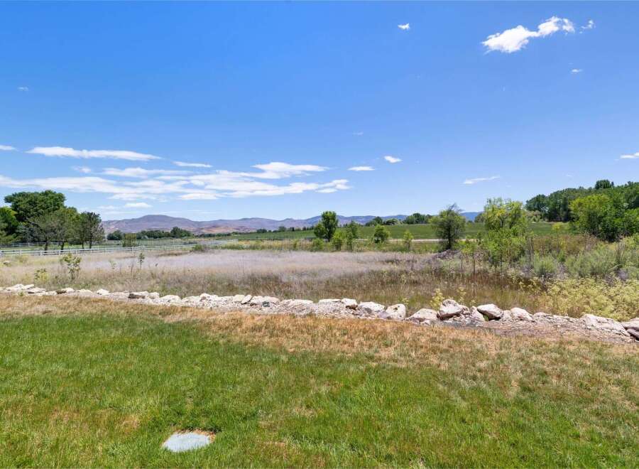 Discover serene country living with this expansive property, featuring rolling hills and distant mountains under a vast blue sky.
