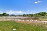 Discover serene country living with this expansive property, featuring rolling hills and distant mountains under a vast blue sky.