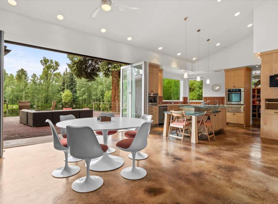 Experience seamless indoor-outdoor living in this stunning modern home, featuring a spacious open-concept kitchen and dining area that flows directly onto a covered patio overlooking a serene lake and lush greenery.