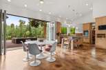 Experience seamless indoor-outdoor living in this stunning modern home, featuring a spacious open-concept kitchen and dining area that flows directly onto a covered patio overlooking a serene lake and lush greenery.