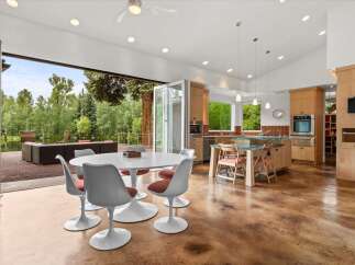 Experience seamless indoor-outdoor living in this stunning modern home, featuring a spacious open-concept kitchen and dining area that flows directly onto a covered patio overlooking a serene lake and lush greenery.