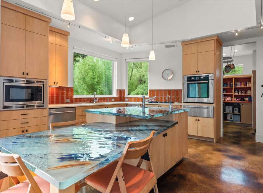 Experience a unique culinary space with this stunning kitchen, featuring a captivating glass island countertop with a mesmerizing water and fish motif.
