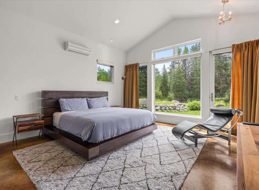 Experience modern luxury in this stunning bedroom featuring a vaulted ceiling and expansive windows that frame breathtaking forest views.