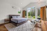Experience modern luxury in this stunning bedroom featuring a vaulted ceiling and expansive windows that frame breathtaking forest views.