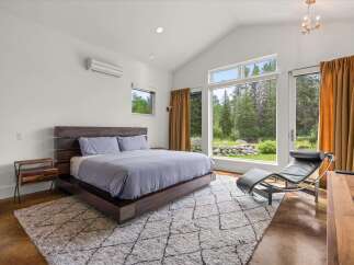 Experience modern luxury in this stunning bedroom featuring a vaulted ceiling and expansive windows that frame breathtaking forest views.