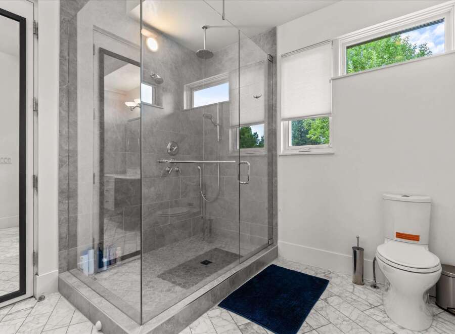 Experience modern luxury in this stunning bathroom featuring a spacious glass-enclosed shower with dual showerheads and elegant grey tilework.