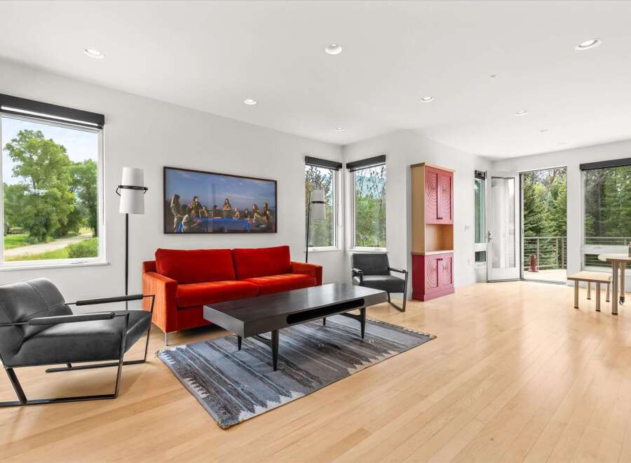 Experience modern living in this bright and airy living room, featuring a vibrant orange sofa and sleek black armchairs.