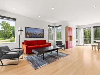Experience modern living in this bright and airy living room, featuring a vibrant orange sofa and sleek black armchairs.