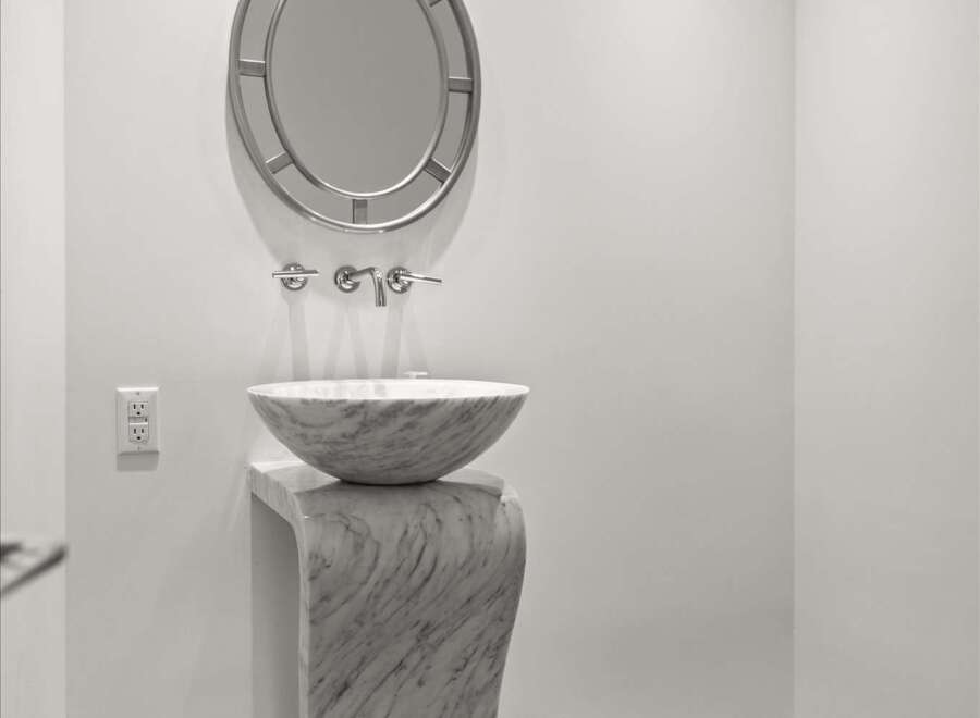 Experience modern elegance in this powder room, featuring a striking marble pedestal sink and a decorative circular mirror.