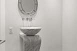 Experience modern elegance in this powder room, featuring a striking marble pedestal sink and a decorative circular mirror.