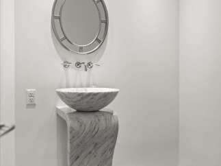Experience modern elegance in this powder room, featuring a striking marble pedestal sink and a decorative circular mirror.