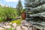 Discover a beautifully landscaped yard featuring a large, rustic planter and a variety of mature trees, including a striking blue spruce.