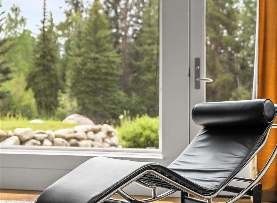 Experience ultimate relaxation in this modern living space, featuring a sleek black leather chaise lounge positioned perfectly to enjoy the breathtaking views.