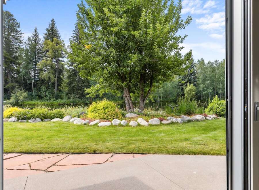 Step outside to a beautifully landscaped backyard featuring a lush green lawn, a serene water feature, and mature trees providing ample shade.