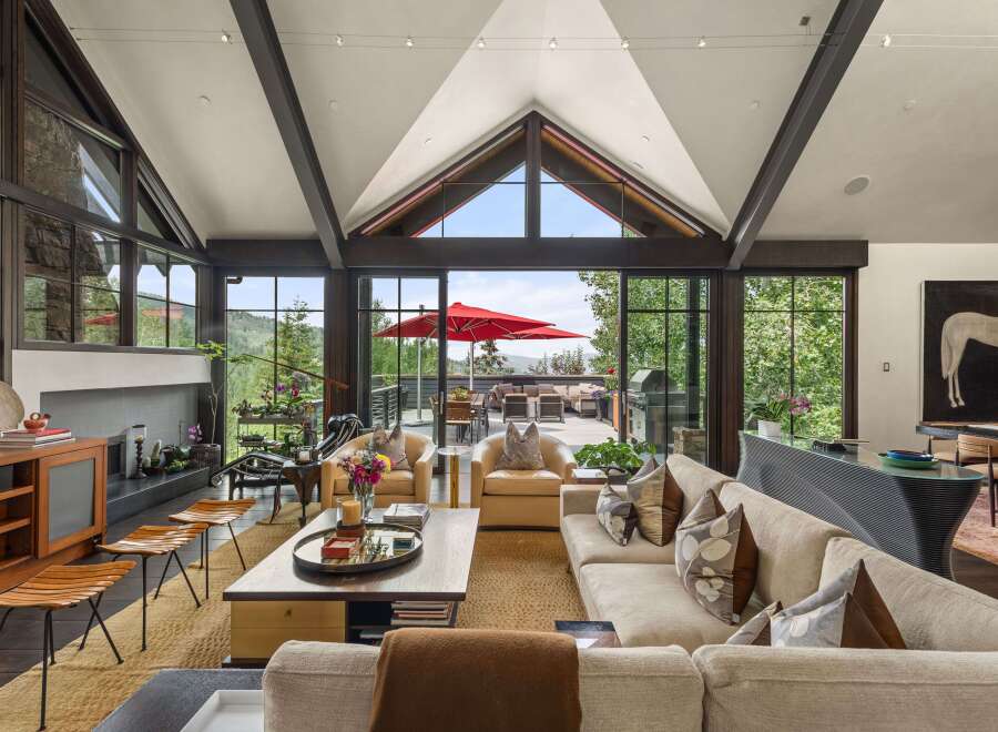 Experience luxurious mountain living in this stunning great room, featuring a soaring vaulted ceiling with exposed beams and a wall of windows offering breathtaking panoramic views.