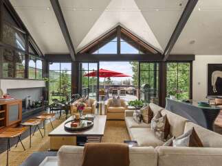 Experience luxurious mountain living in this stunning great room, featuring a soaring vaulted ceiling with exposed beams and a wall of windows offering breathtaking panoramic views.