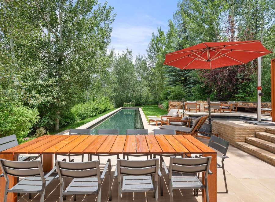 This stunning outdoor living space features a rectangular swimming pool surrounded by lush greenery and a spacious patio.