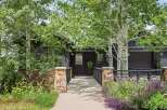 Discover this stunning modern home featuring a dark wood exterior and a welcoming stone pathway leading to the entrance.
