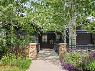 Discover this stunning modern home featuring a dark wood exterior and a welcoming stone pathway leading to the entrance.
